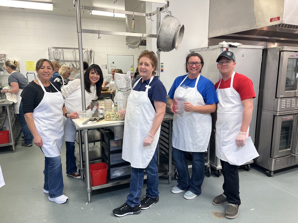A group of people wearing aprons preparing food in a commercial kitchen