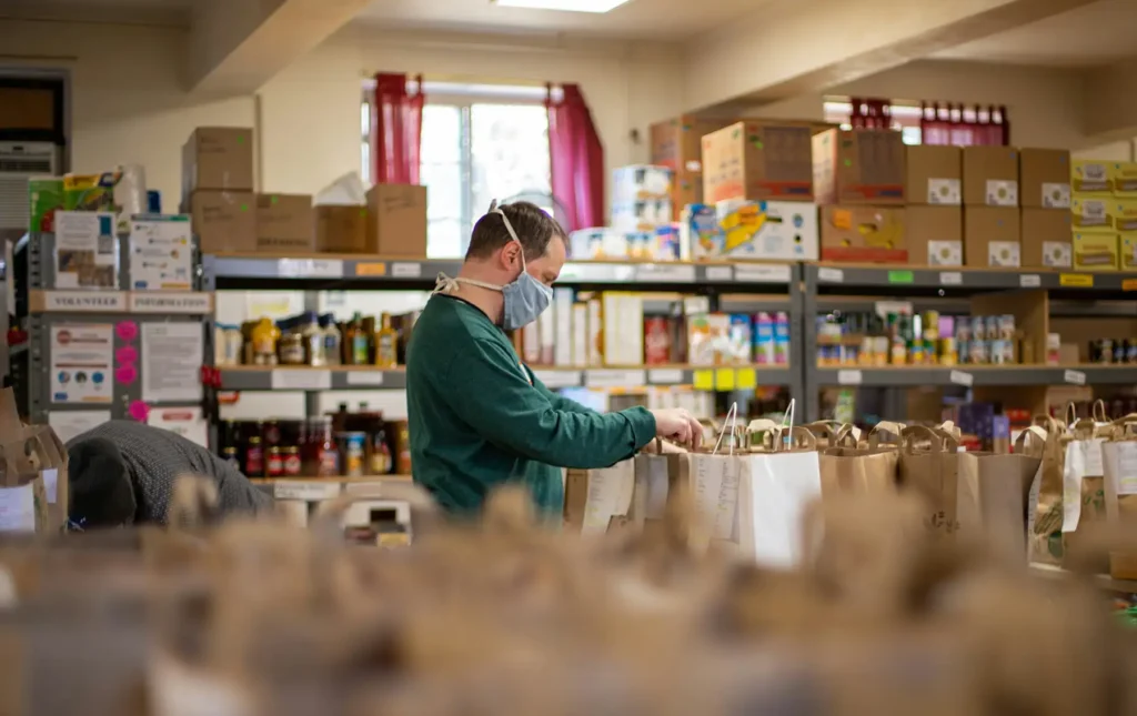 A man wearing a mask organizes bags of food in a food pantry.