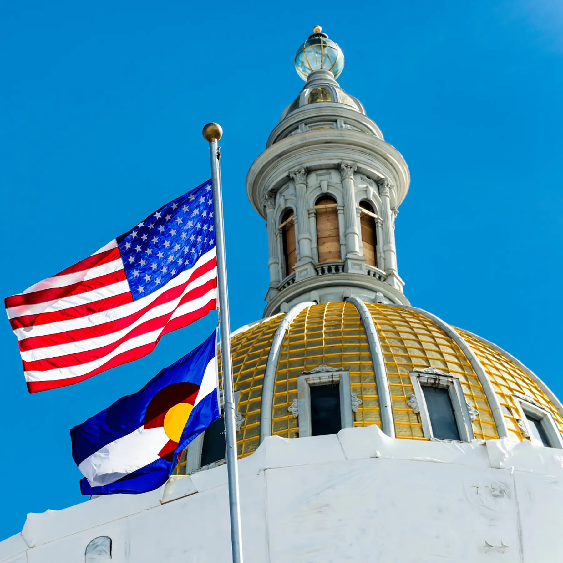 The American and Colorado State flag waving in front of the Colorado state capitol building